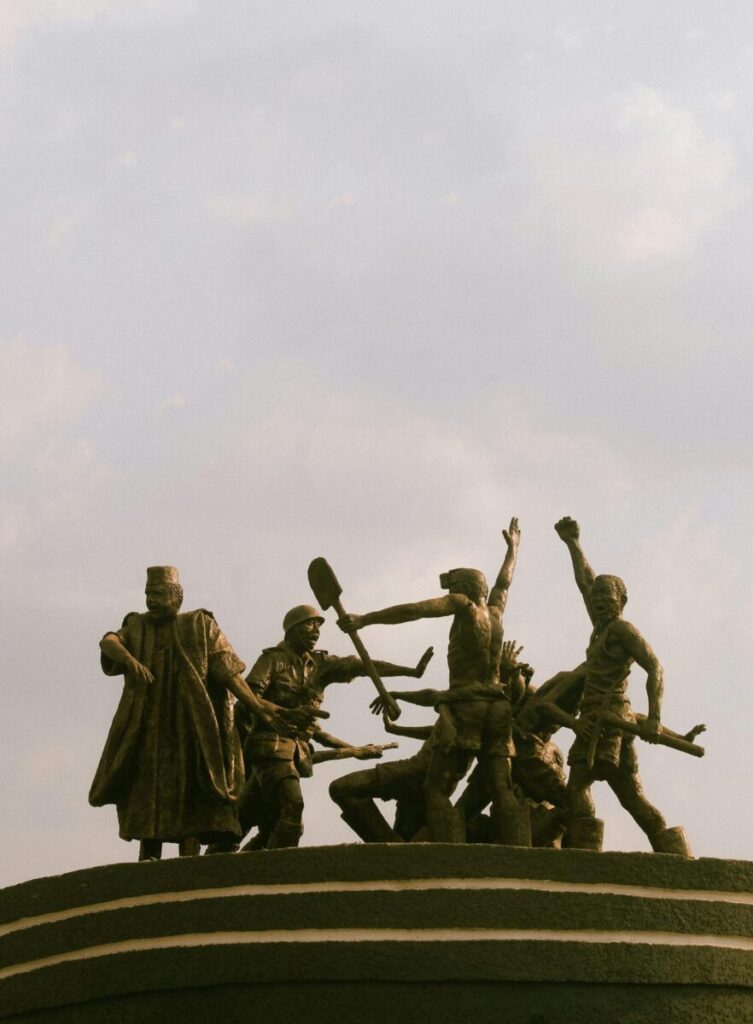 A striking bronze statue depicting historical figures in Enugu, Nigeria, against a cloudy sky.